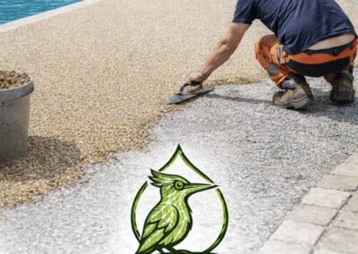 Poseur réalisant la mise en œuvre d’une moquette de pierre sur terrasse extérieure, logo Woodpecker Paysage en bas de page, chantier en Seine-et-Marne